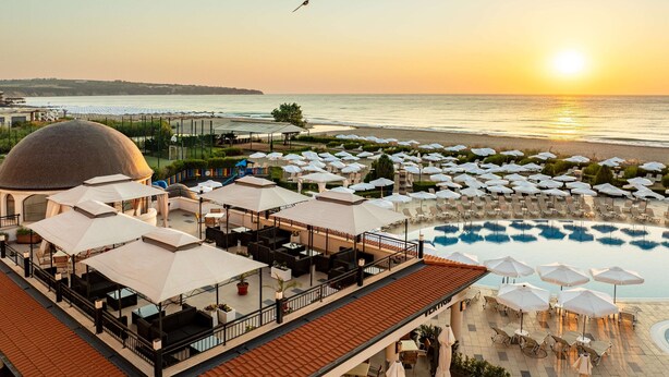 A rooftop pool area with lounge chairs and umbrellas, overlooking the sea at sunset. -  Alua Helios Bay - All Inclusive (Obzor)