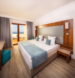 A hotel room with a large bed, a desk, and a view of the sea through the balcony.