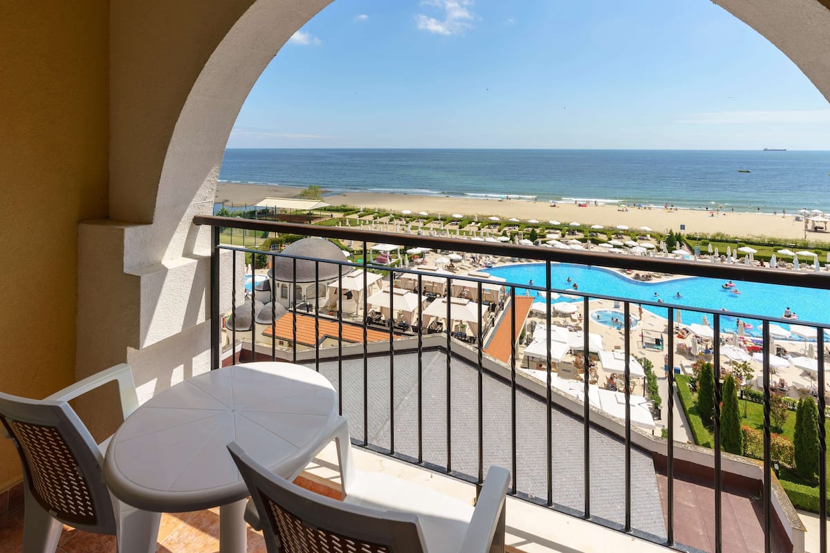 A balcony with a view of a beach and a swimming pool.