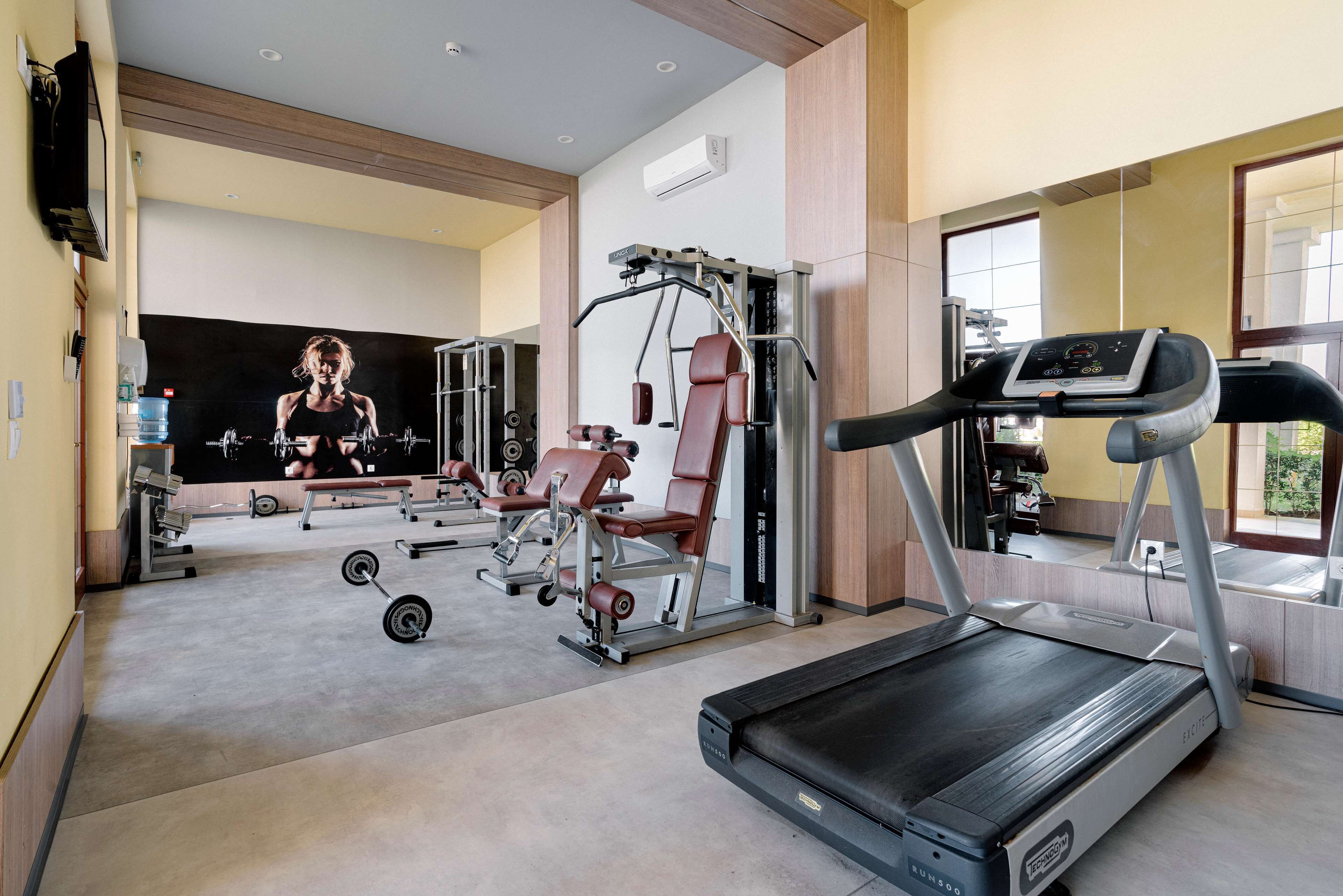 Un gimnasio moderno con cinta de correr, máquinas de pesas y un espejo grande.