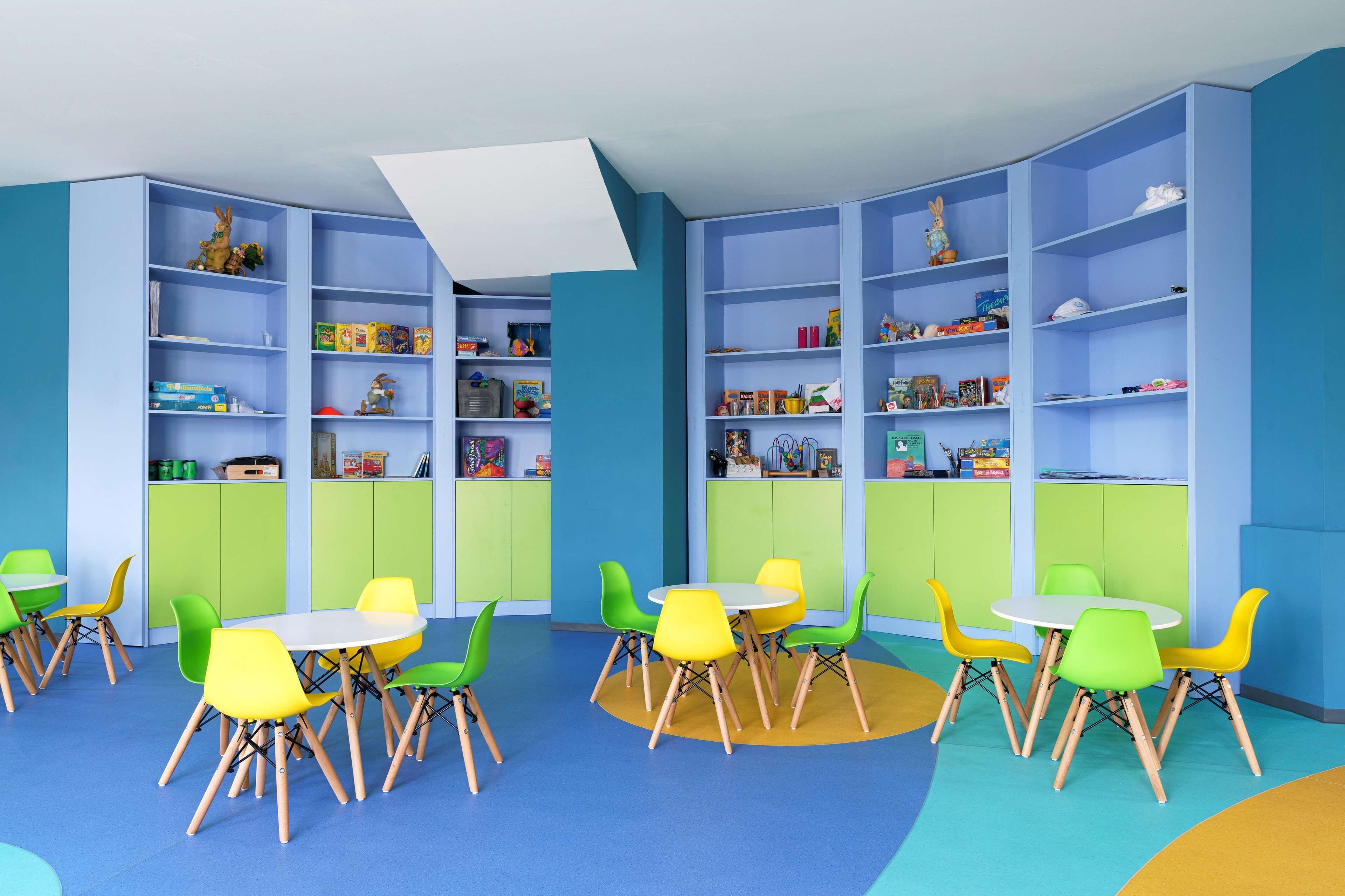 Un salón de juegos infantiles con sillas y mesas de colores, y estanterías llenas de juguetes y libros.