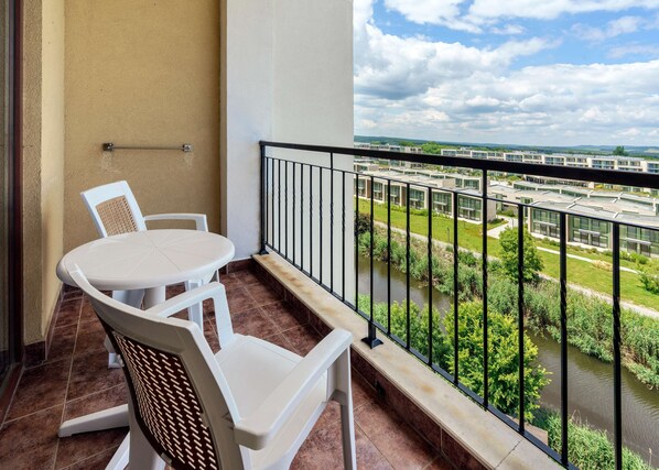 A balcony with a table and chairs, a view of a river, and modern buildings in the background.