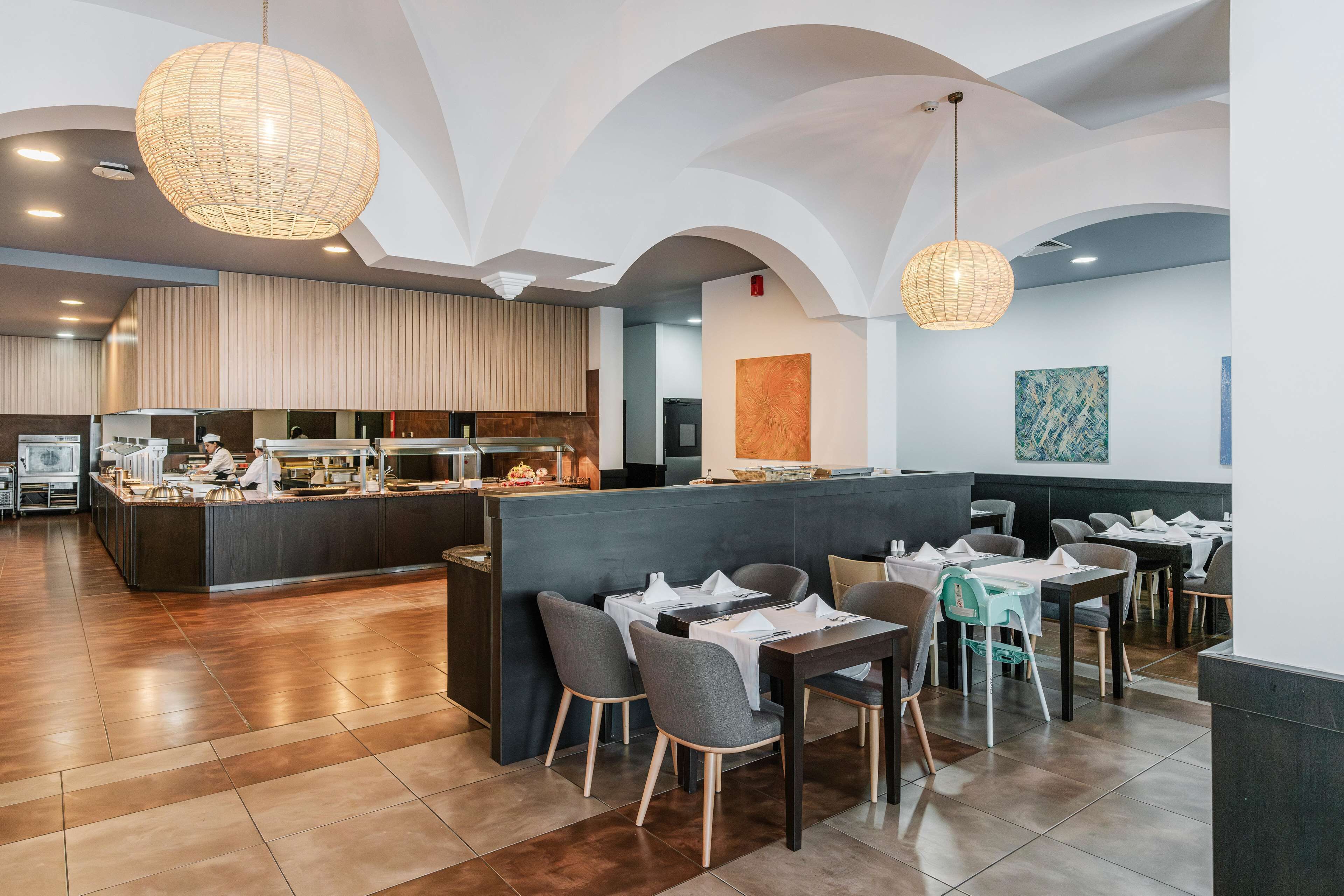Um restaurante moderno com balcão central, área de refeições com mesas e cadeiras, e cozinha ao fundo.