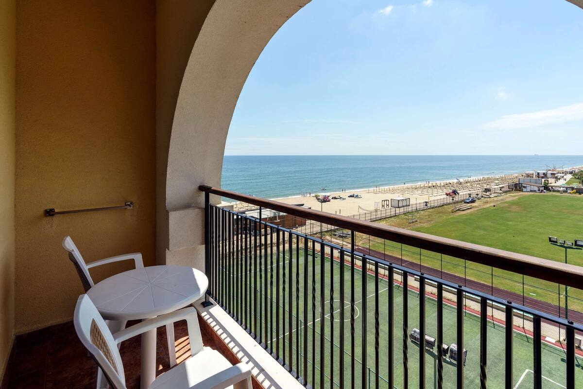 A balcony with a view of the beach and a sports field.