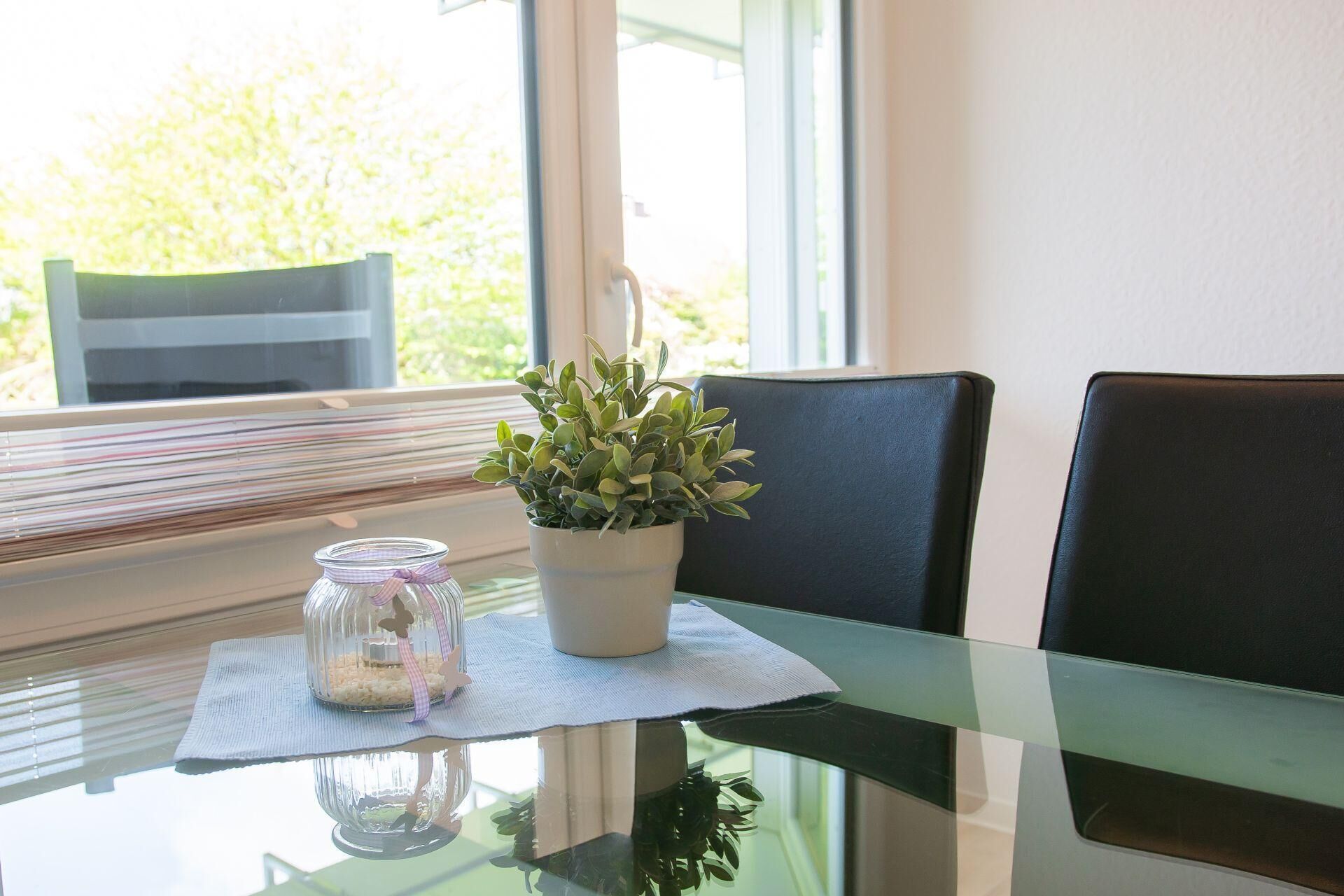 A glass table with a potted plant and a glass jar with a ribbon.