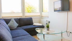A modern living room with a sectional sofa, a glass coffee table, and a flat-screen TV mounted on the wall. - "Dünengras" in the Strandburg house... close to the beach and in a quiet location! (Dahme)