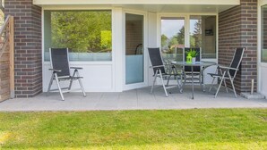 A covered patio with a glass door, two black chairs, and a small table with a plant. - "Dünengras" in the Strandburg house... close to the beach and in a quiet location! (Dahme)