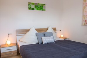 Un lit bien fait, recouvert d’une couvre-lit à motifs sombres, deux tables de chevet avec des lampes et une œuvre d’art murale au-dessus du lit.