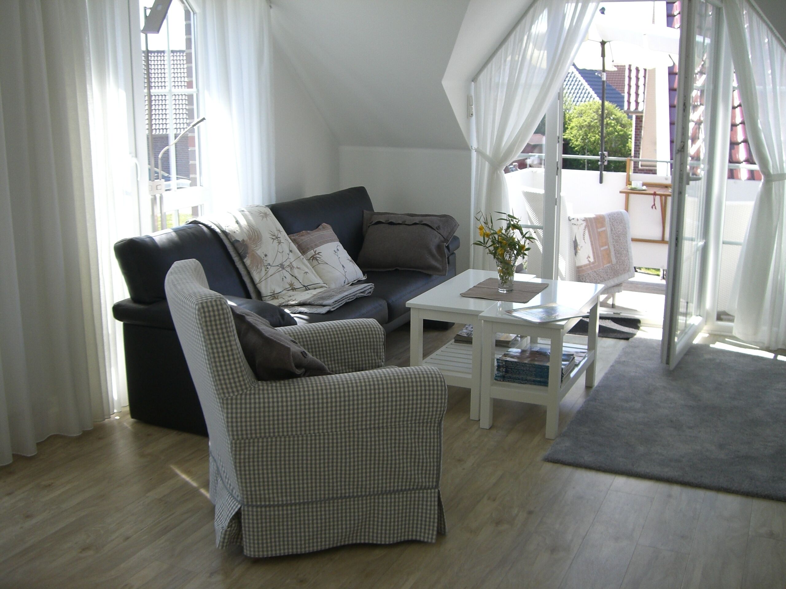 A living room with a sofa, armchair, coffee table, and a view of the outside.