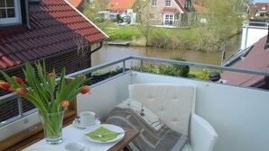 Ein Balkon mit einem Tisch für zwei Personen, einer Tulpenvase und Blick auf einen Fluss und Häuser im Hintergrund.