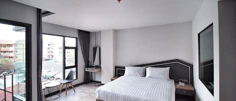 A modern hotel room with a large bed, a desk, a chair, and a balcony with a view of the city.