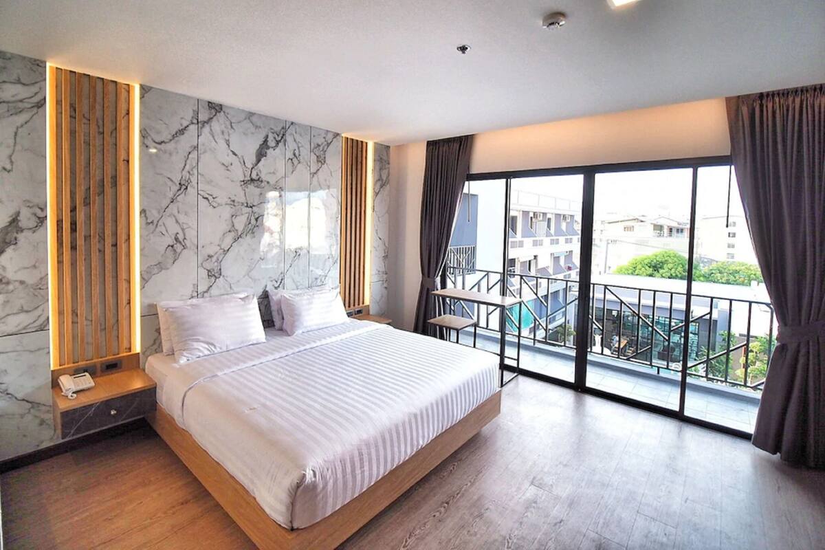 A modern hotel room with a large bed, marble wall, wooden accents, and a balcony with a city view.