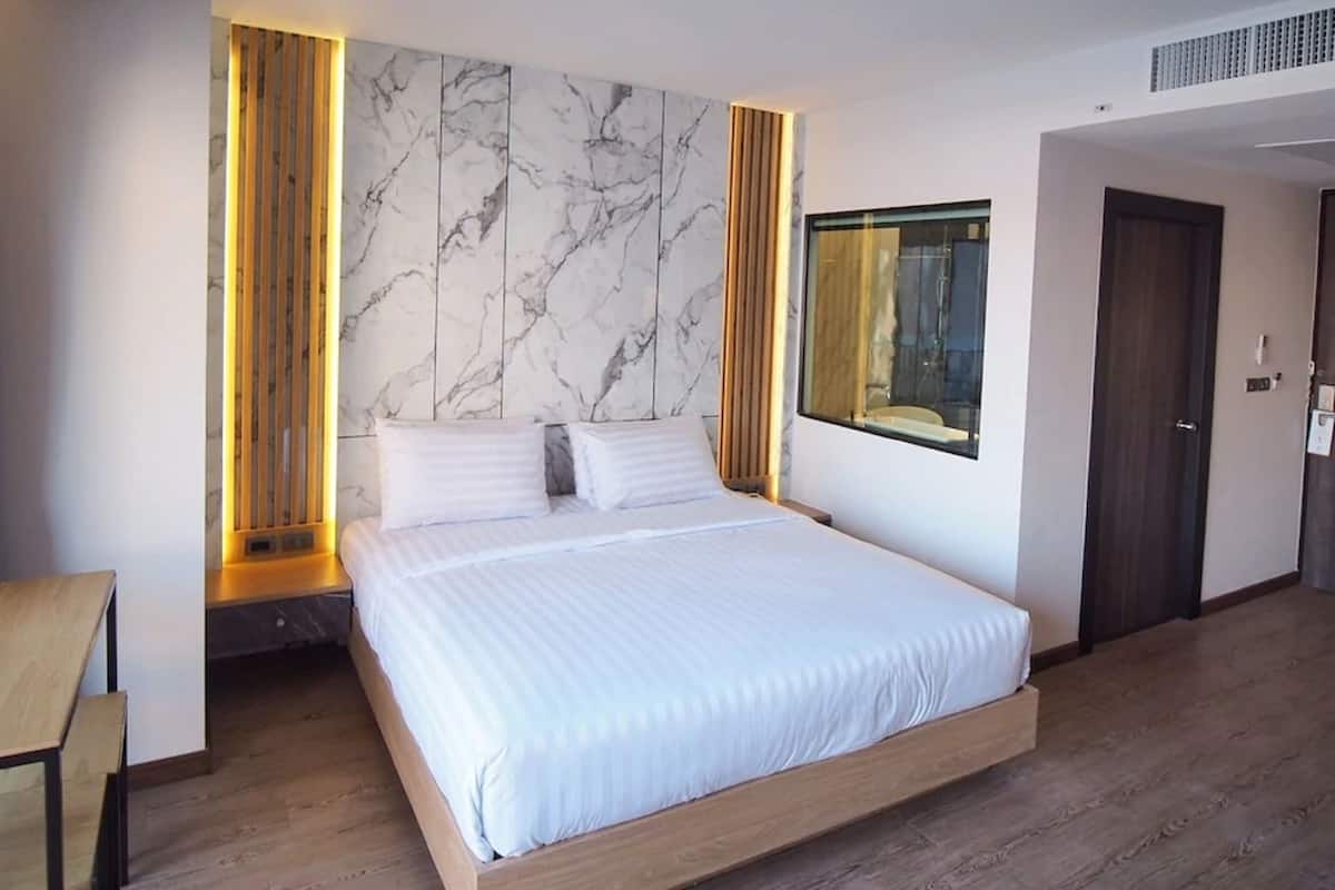 A modern hotel room with a large bed, wooden floor, marble-patterned wall, and a large window.