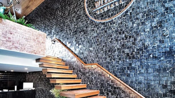 Eine moderne Treppe mit Holzbeschlägen und einem Metallgeländer, die zu einem Empfangsbereich mit schwarz-weiß kariertem Boden führt.