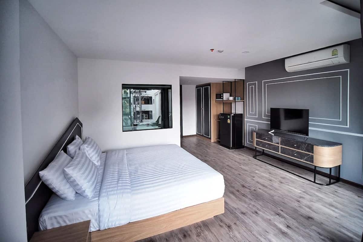 A modern hotel room with a large bed, a TV, a minibar, and a view of the outside.