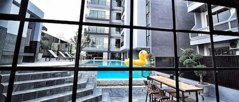 En modern byggnad med en pool, utomhusmöbler och utsikt över ett bostadsområde.
