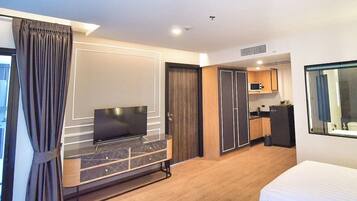 A hotel room with a bed, a TV, a minibar, a small kitchen area, and a bathroom with a mirror.