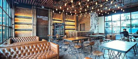 A spacious cafe with leather seating, exposed brick walls, and a high ceiling with hanging lights.