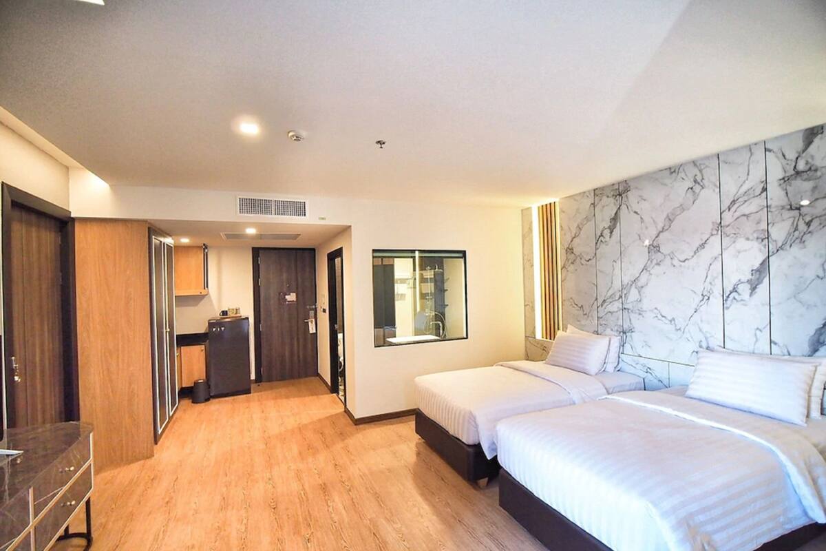 A hotel room with a wooden floor, two beds, a marble wall, and a small kitchenette.