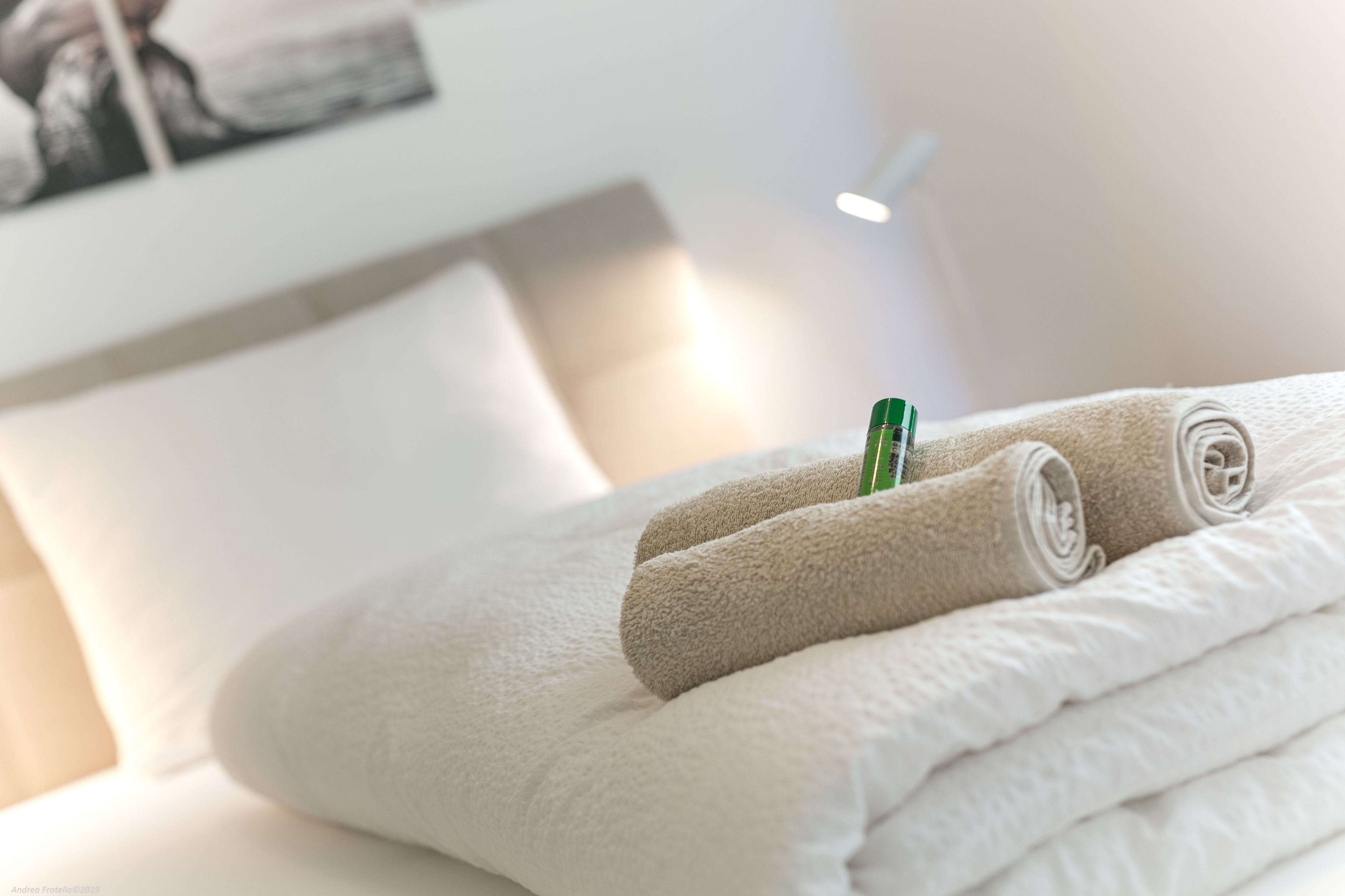 Un letto rifatto con asciugamani arrotolati e una bottiglia verde sopra.