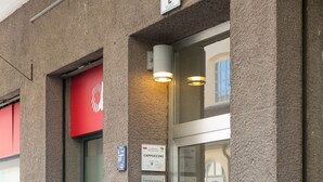 A hotel entrance with a glass door, a red awning, and a sign indicating "Cappuccino" and "Duomo" amenities. - Apartment Duomo (Bolzano)