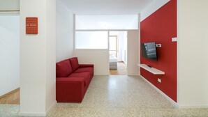 A modern living room with a red sofa, a flat-screen TV mounted on a red wall, and a small white shelf. - Apartment Duomo (Bolzano)