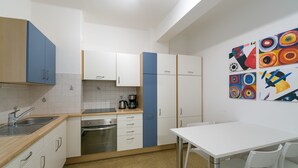 A modern kitchen with white cabinets, a coffee machine, and a dining area with a white table and chairs. - Apartment Duomo (Bolzano)