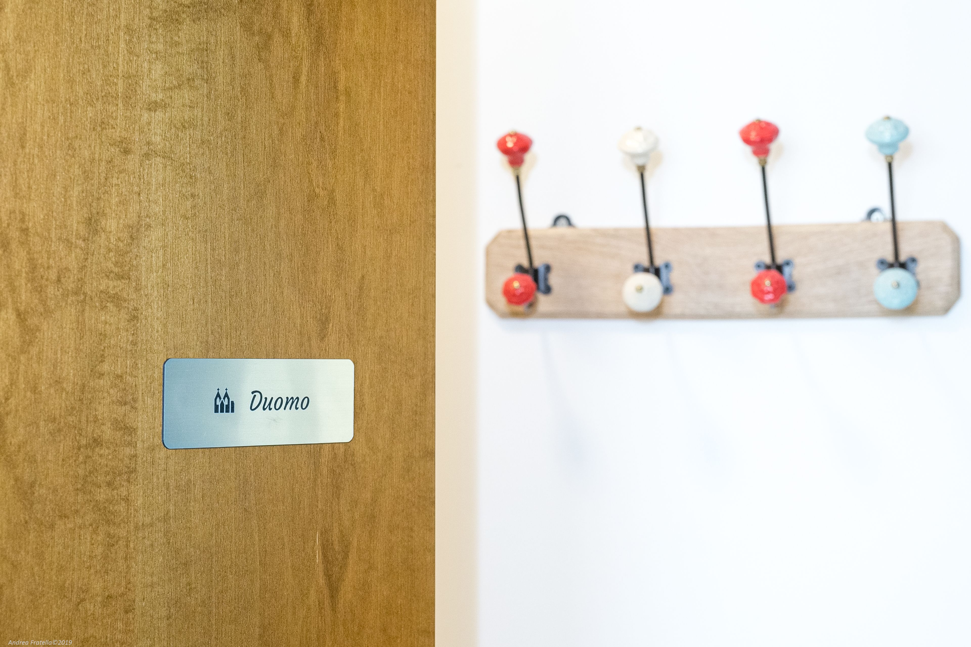Una puerta de madera con una placa que dice "Duomo" y un panel de ganchos de colores colgado en la pared.