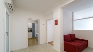 A modern room with a red sofa, a coffee machine, and a kitchen area visible through an open door. - Apartment Duomo (Bolzano)