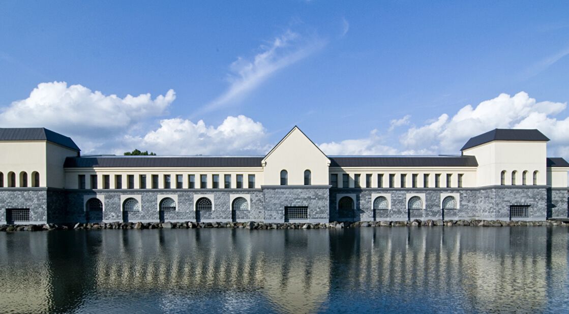 Ein großes Gebäude mit einem zentralen, dreieckigen Teil und zahlreichen Rundbogenfenstern entlang der Seiten.
