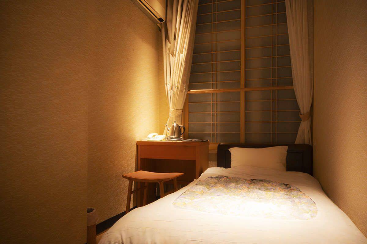 Une chambre à coucher avec un lit, une table de chevet, une chaise et une fenêtre avec des rideaux.