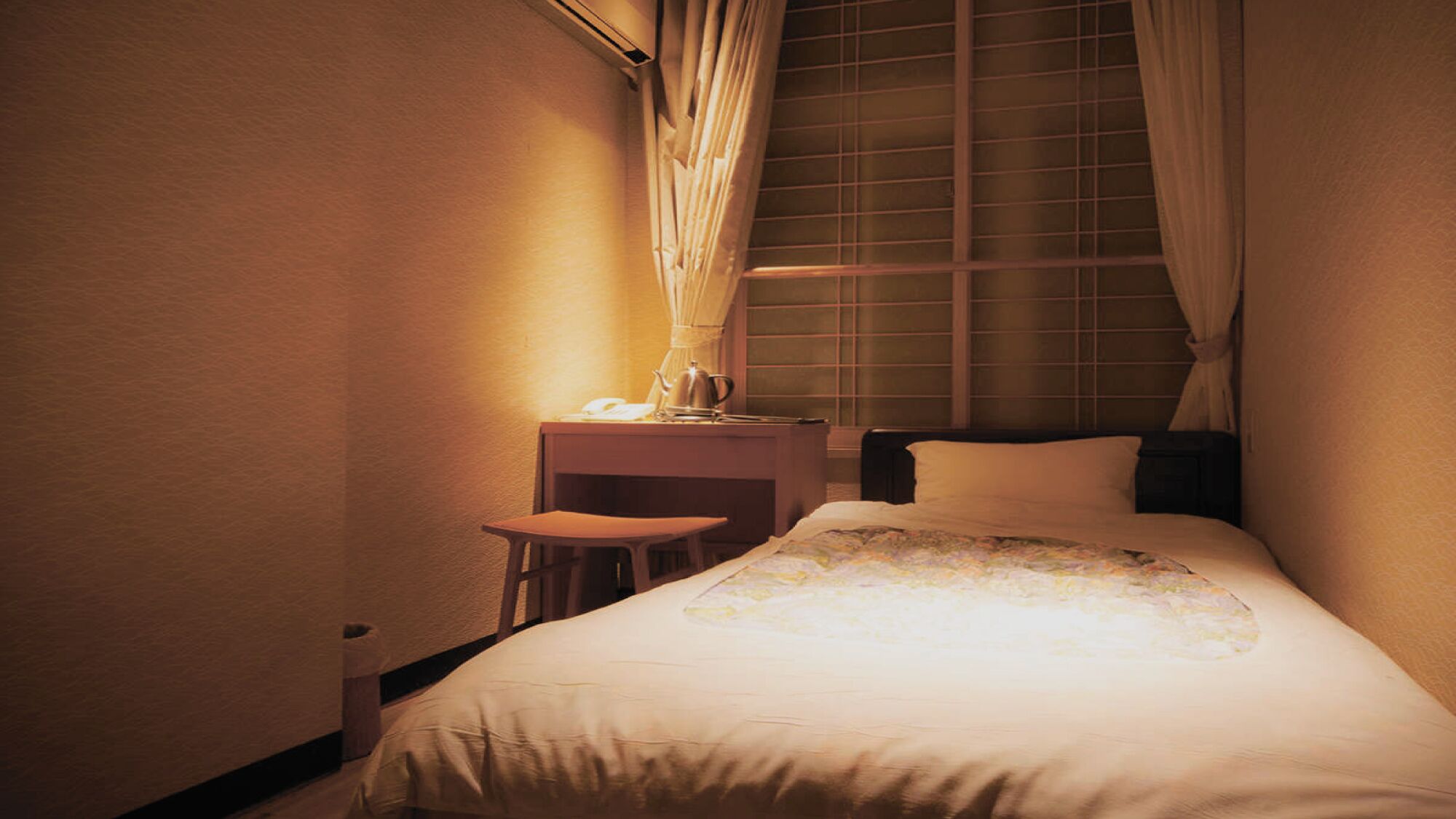 Ein Hotelzimmer mit Bett, Nachttisch, kleinem Tisch und einem Fenster mit Vorhängen.