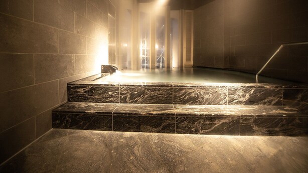 Un espace spa avec des marches en marbre menant à un jacuzzi, entouré de murs et éclairé par un luminaire au plafond.