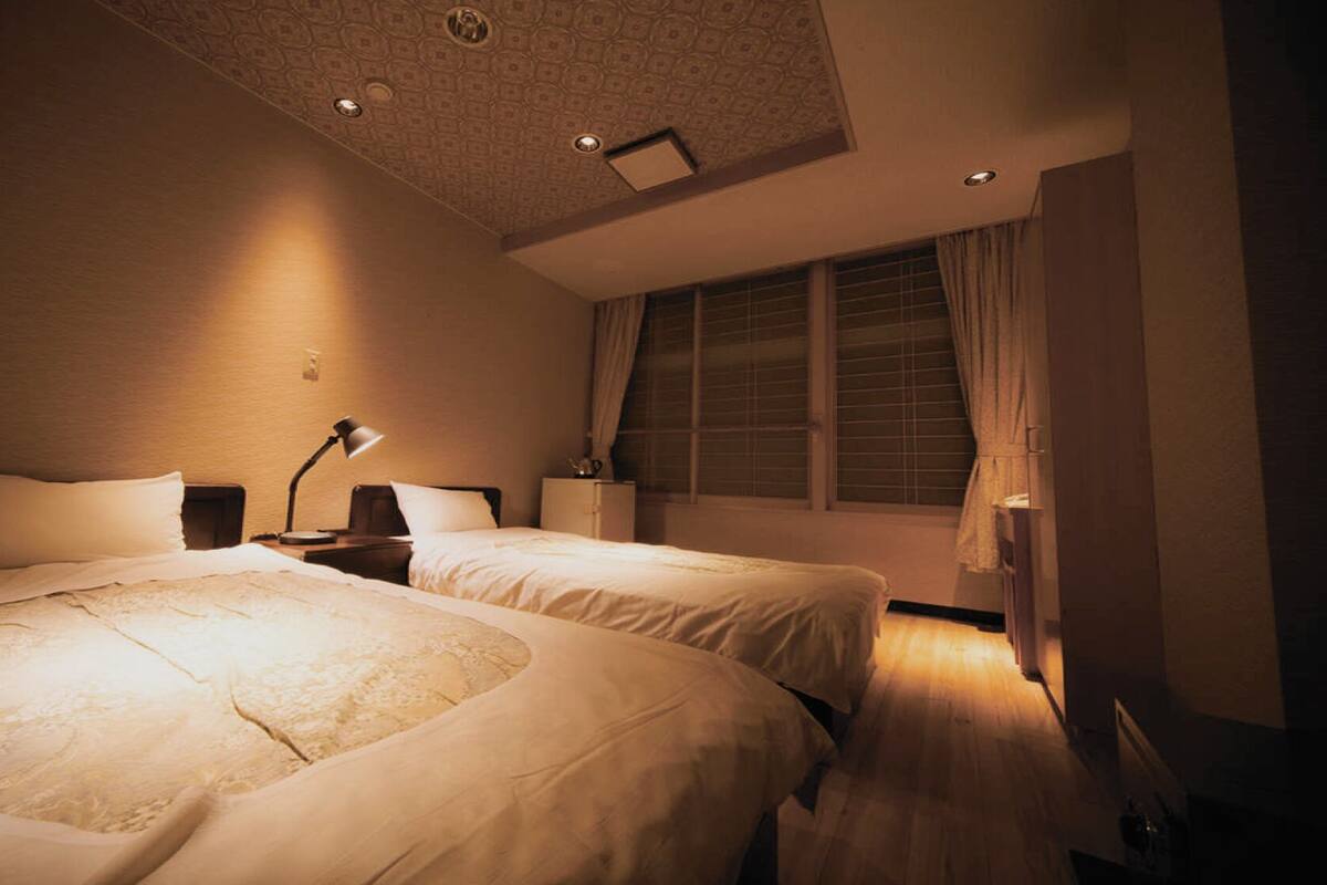 Une chambre d’hôtel avec deux lits, un bureau, une lampe, une fenêtre avec des rideaux et un plafond décoré de motifs.
