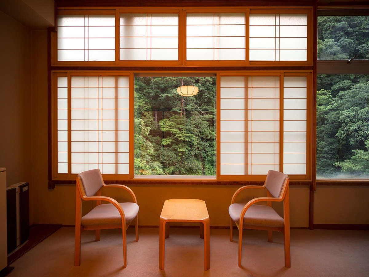 Une pièce dotée d’une fenêtre à panneaux coulissants de style japonais traditionnel, de deux chaises en bois et d’une petite table.