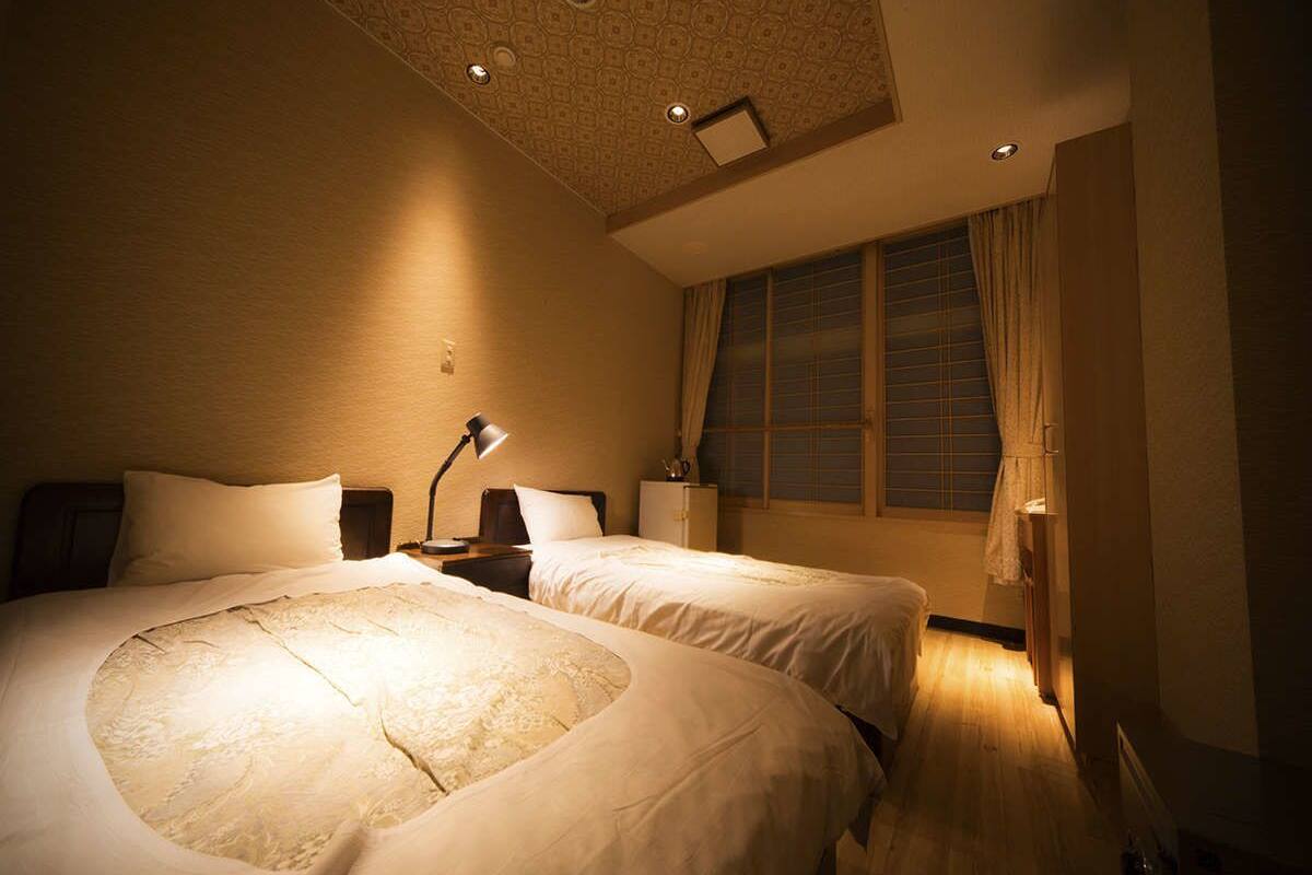 Une chambre avec deux lits, une table de chevet, une lampe, une fenêtre avec des rideaux et un plafond à motifs.