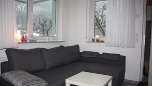 Moderni olohuone, jossa on tummanharmaa sohva, valkoinen sohvapöytä ja kaksi ikkunaa, joissa on valkoiset verhot.
