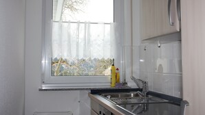 Keittiössä on ikkuna, ruostumattomasta teräksestä valmistettu pesuallas ja valkoiset kaapit.
