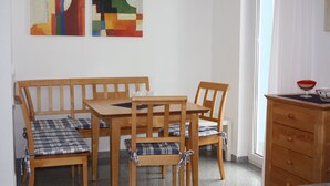 Ruokailutilassa on puinen pöytä ja tuolit, pieni kaappi sekä kaksi abstraktia maalausta seinällä.