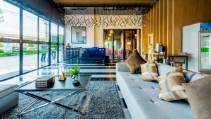Een moderne lobby met een receptiebalie, een zithoek en grote ramen met uitzicht op buiten.