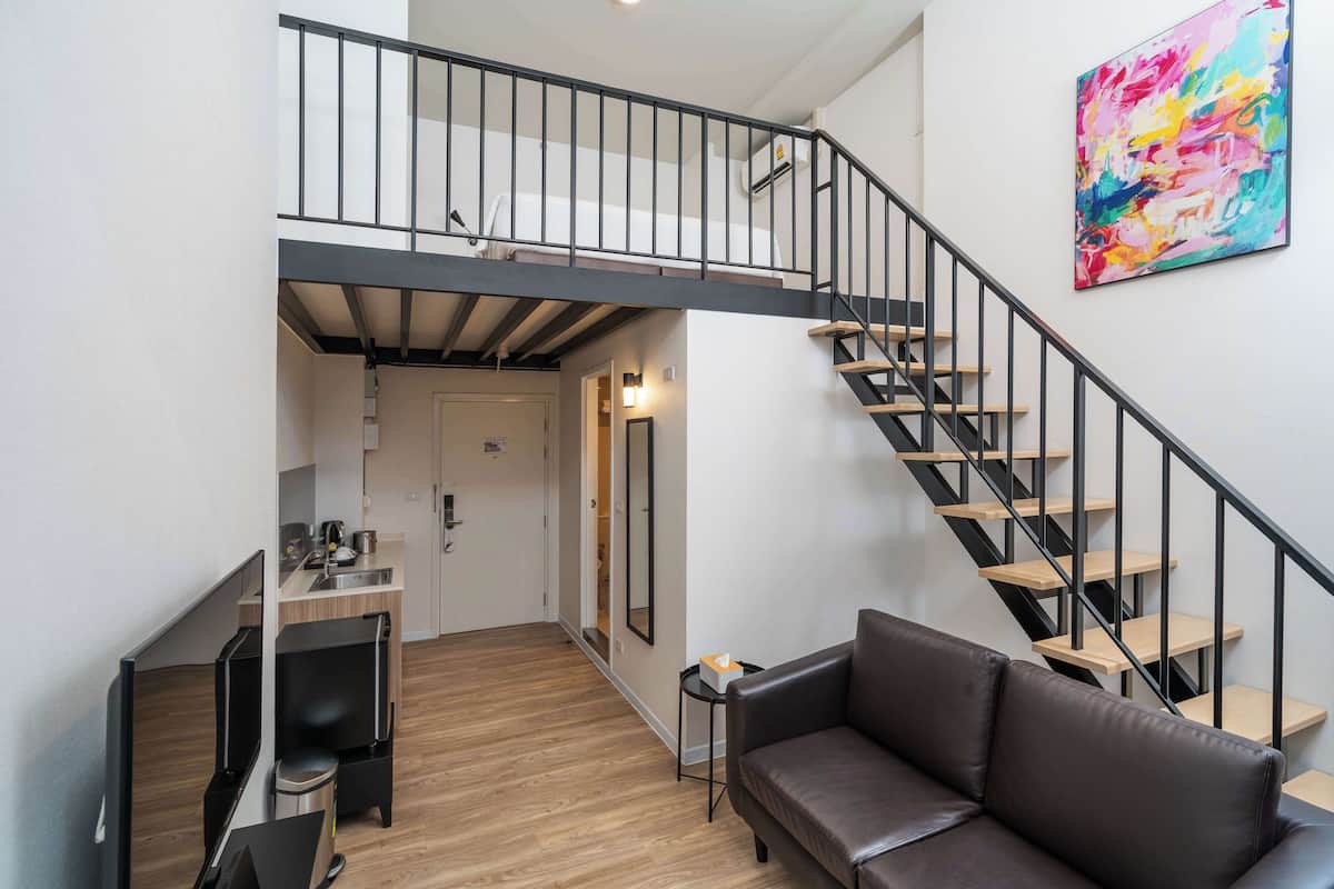A modern apartment with a loft bedroom, a kitchen area, and a staircase.