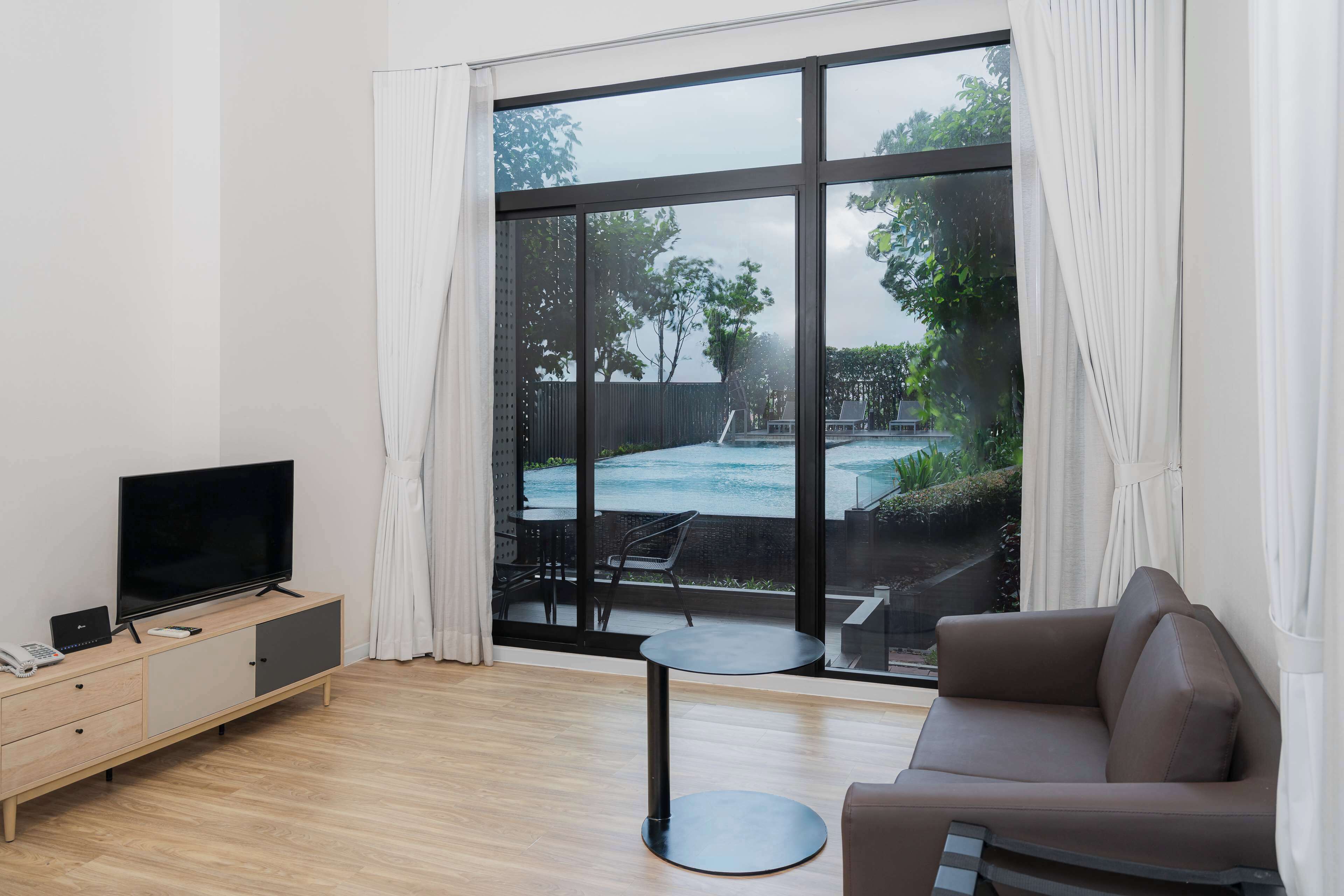 Un soggiorno moderno con un'ampia finestra, una TV a schermo piatto su un mobile in legno, un tavolino rotondo e un divano marrone.