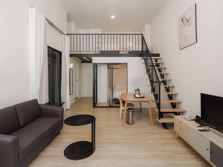 Una sala de estar moderna con sofá, una mesa de comedor, un televisor y una escalera que sube a un nivel superior.