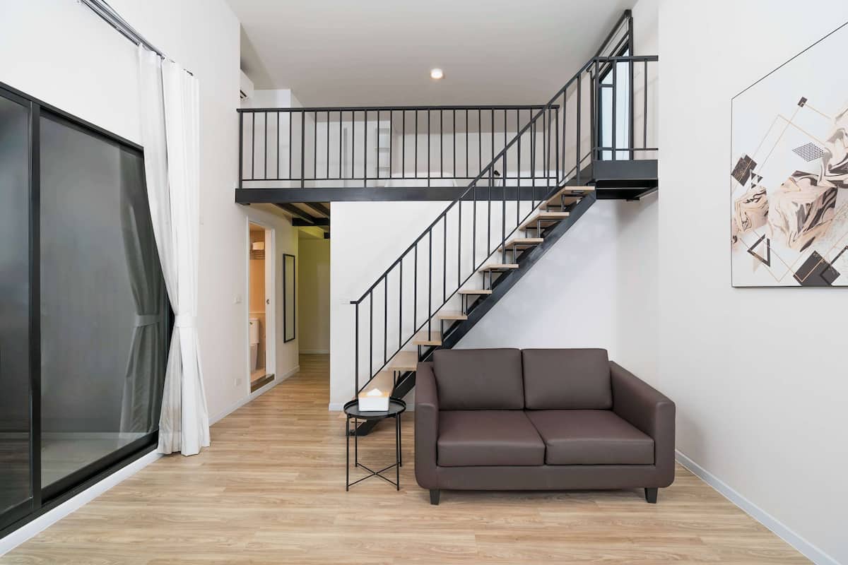 A modern living room with a brown sofa, a small side table, a staircase with a black railing, and a large abstract painting on the wall.