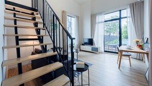 Een moderne woonkamer met een houten trap, een eetgedeelte en een groot raam met gordijnen.