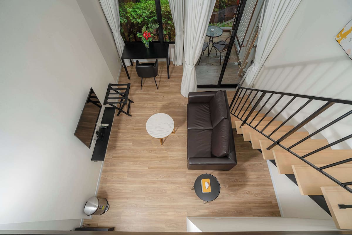 A modern living area with a sofa, coffee table, and dining table. A staircase leads to an upper level.