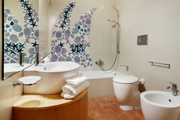 A bathroom with a bathtub, a toilet, a bidet, a sink, and a mirror.