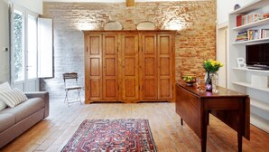 Een kamer met een houten garderobe, een bank, een tafel met een vaas en fruit, en een boekenkast.