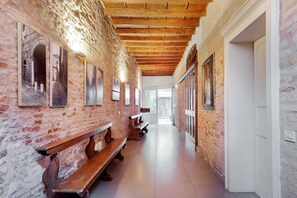 A corridor with exposed brick walls, wooden benches, and framed pictures on the walls. - GuestHost - The medieval home of the Duke! In the historic center (Ferrara)