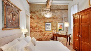 Een slaapkamer met een groot bed, een houten kledingkast, een bakstenen muur en omlijste kunstwerken.